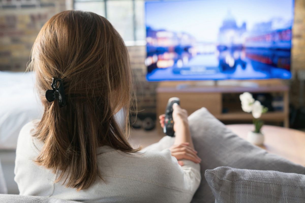 Mulher faz ajuste usando conreole remoto para melhorar sinal da tv ilustra nosso artigo Fazendo o Ajuste fino para melhorar a qualidade do sinal da TV.