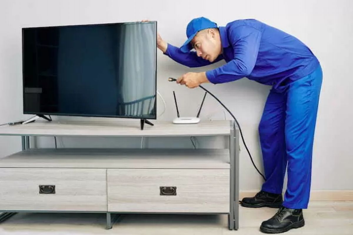 Técnico conectando cabo de antena na televisão ilustra nosso artigo sobre atualização de equipamentos e cabos: garantindo a integridade do sinal de TV.