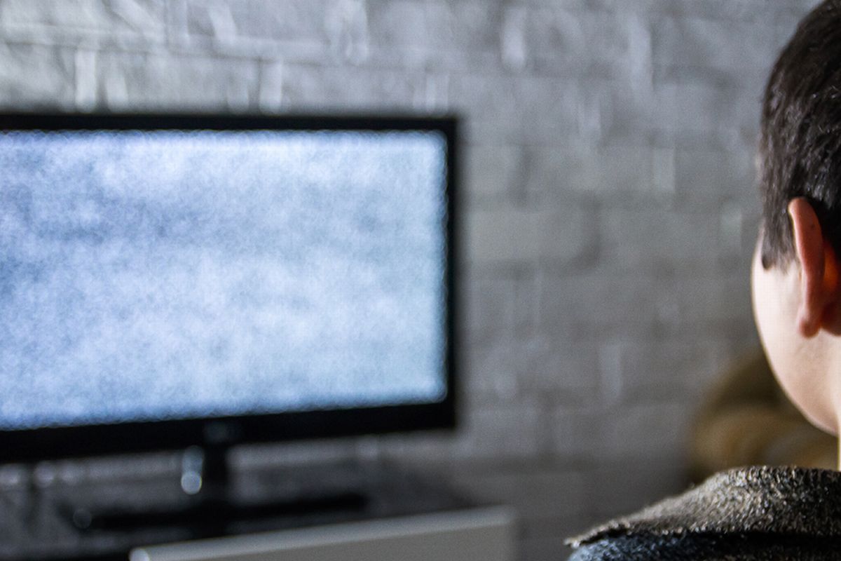 Um menino olhando para a TV sem sinal ilustra nosso artigo sobre condições climáticas que interferem no sinal da TV digital.