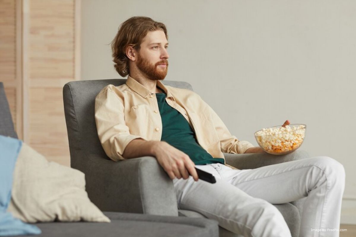 Um homem sentando na poltrona segurando controle remoto da TV ilustra nosso artigo sobre: Sobre a fonte de energia dos controles remotos.