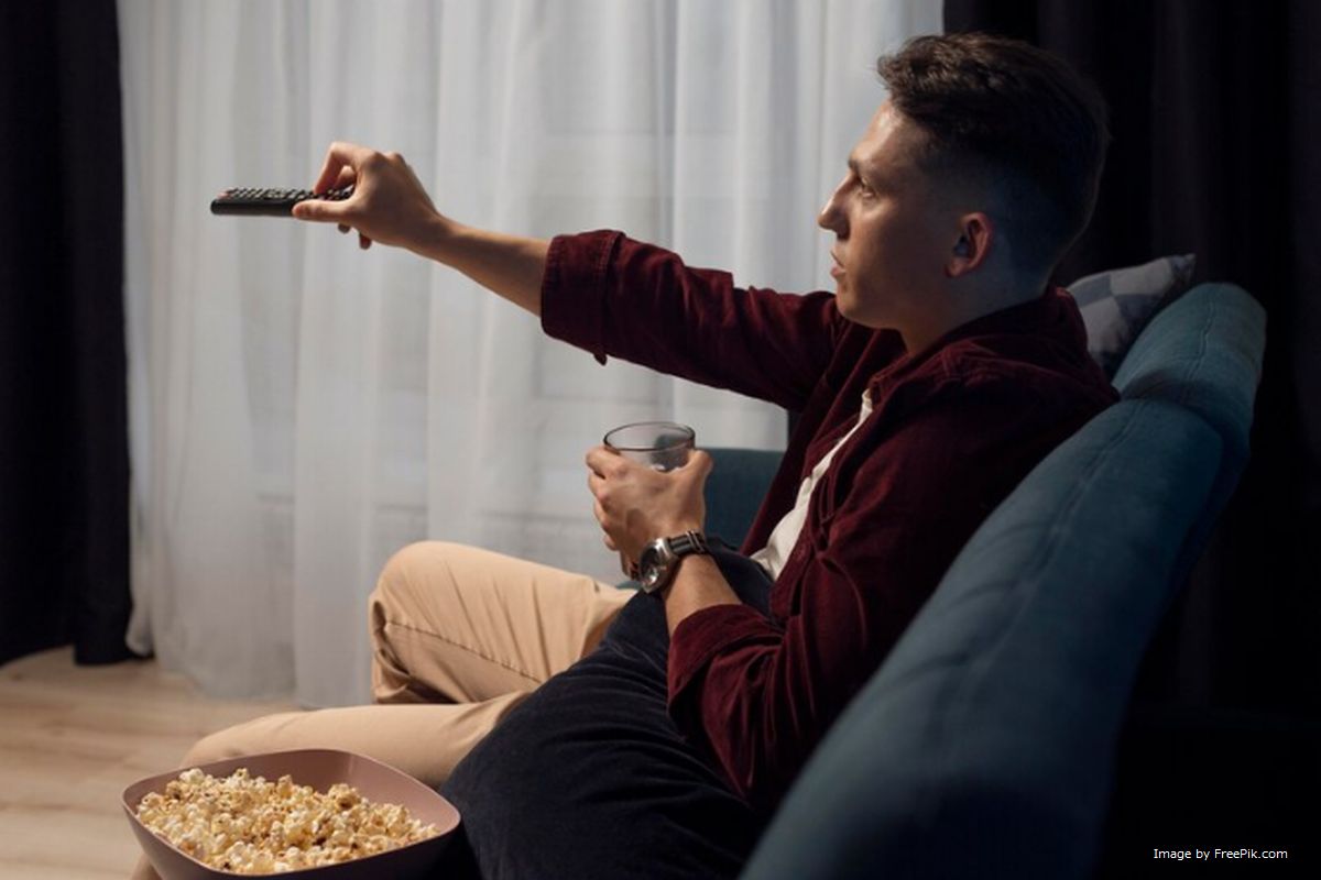 Um homem sentando no sofá segurando controle remoto da TV ilustra nosso artigo sobre: Facilidade de uso do controle remoto.
