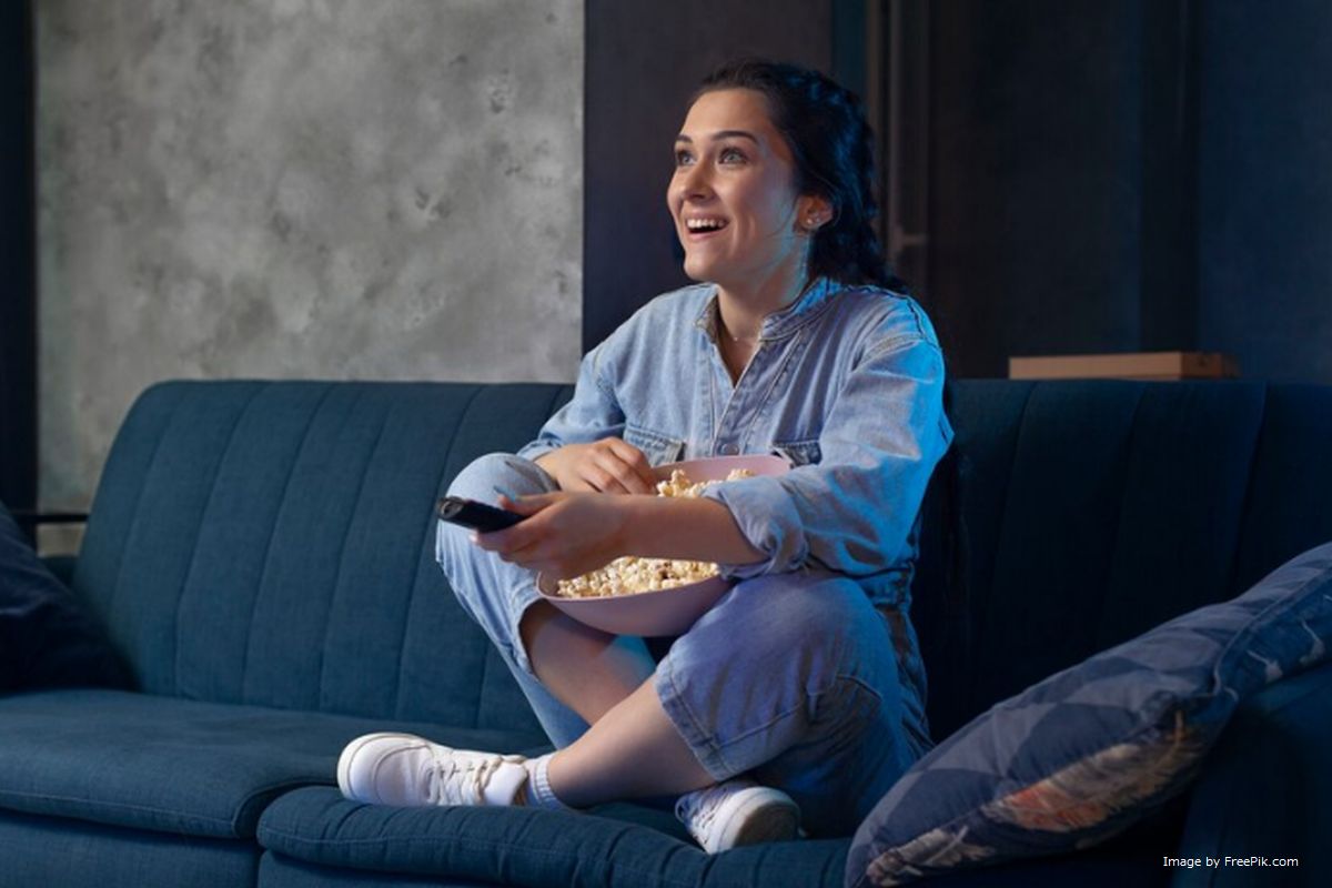 Uma mulher sentanda no sofá segurando controle remoto da TV ilustra nosso artigo sobre: A tecnologia por trás da conectividade dos controles remotos.